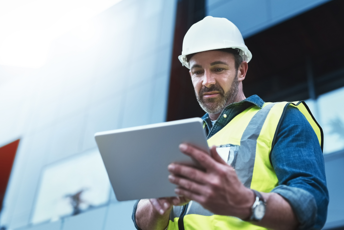 A male construction worker outside looking at a tablet