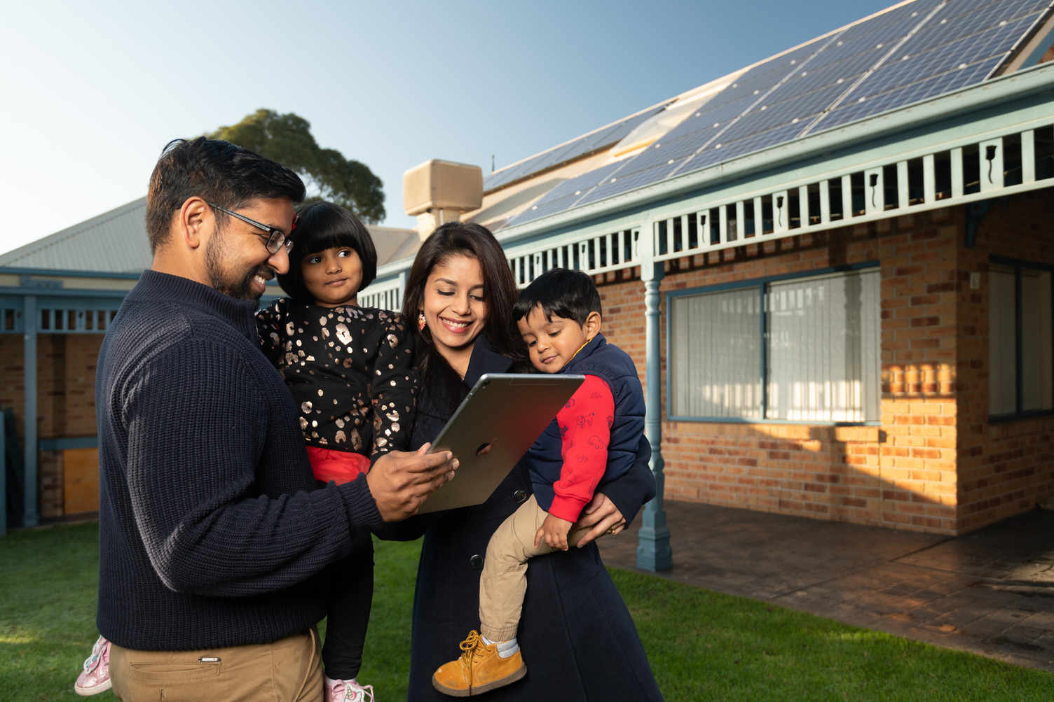 A family outside looking at a tablet screen near a solar panel