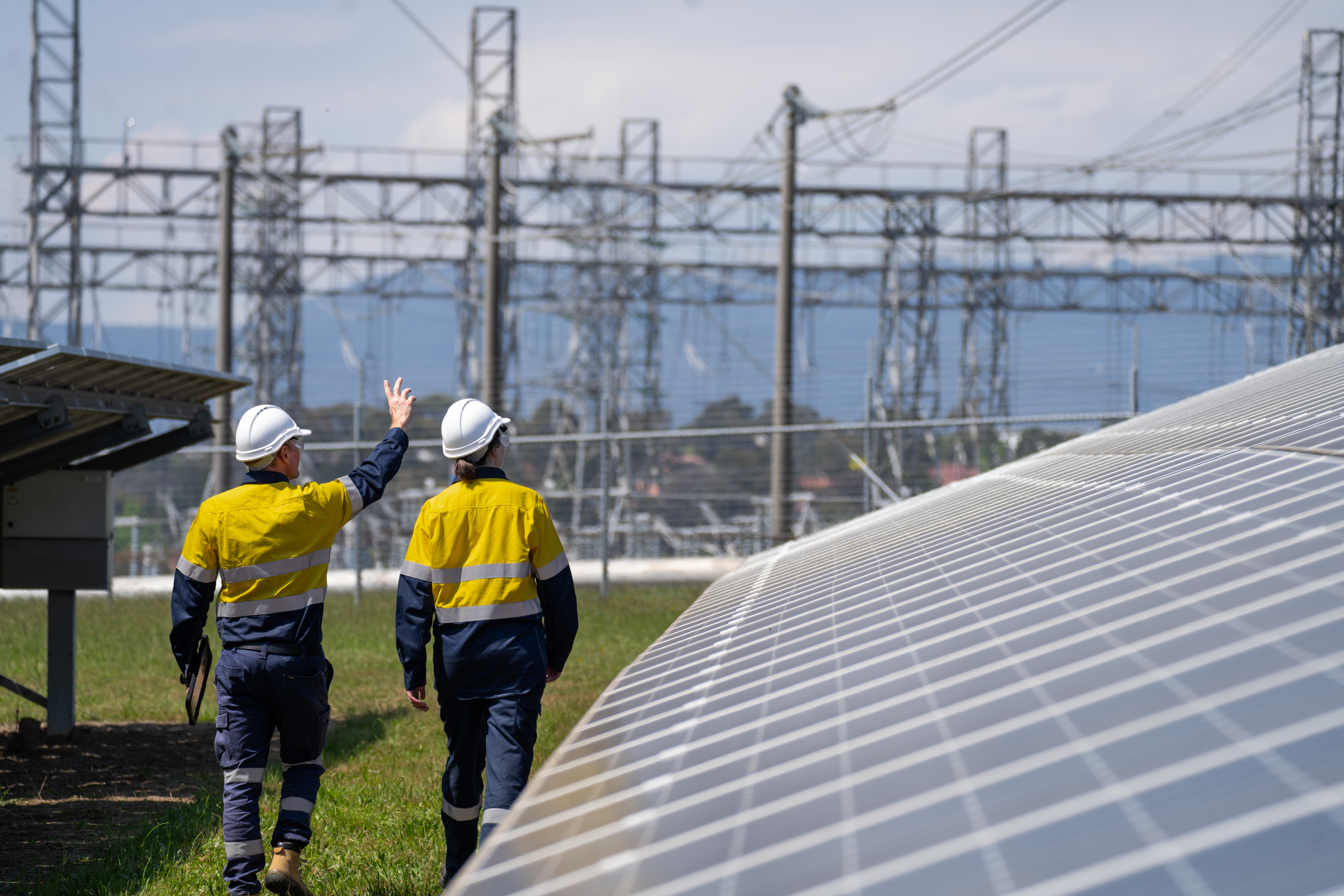 Two workers walking outside next to a solar panel